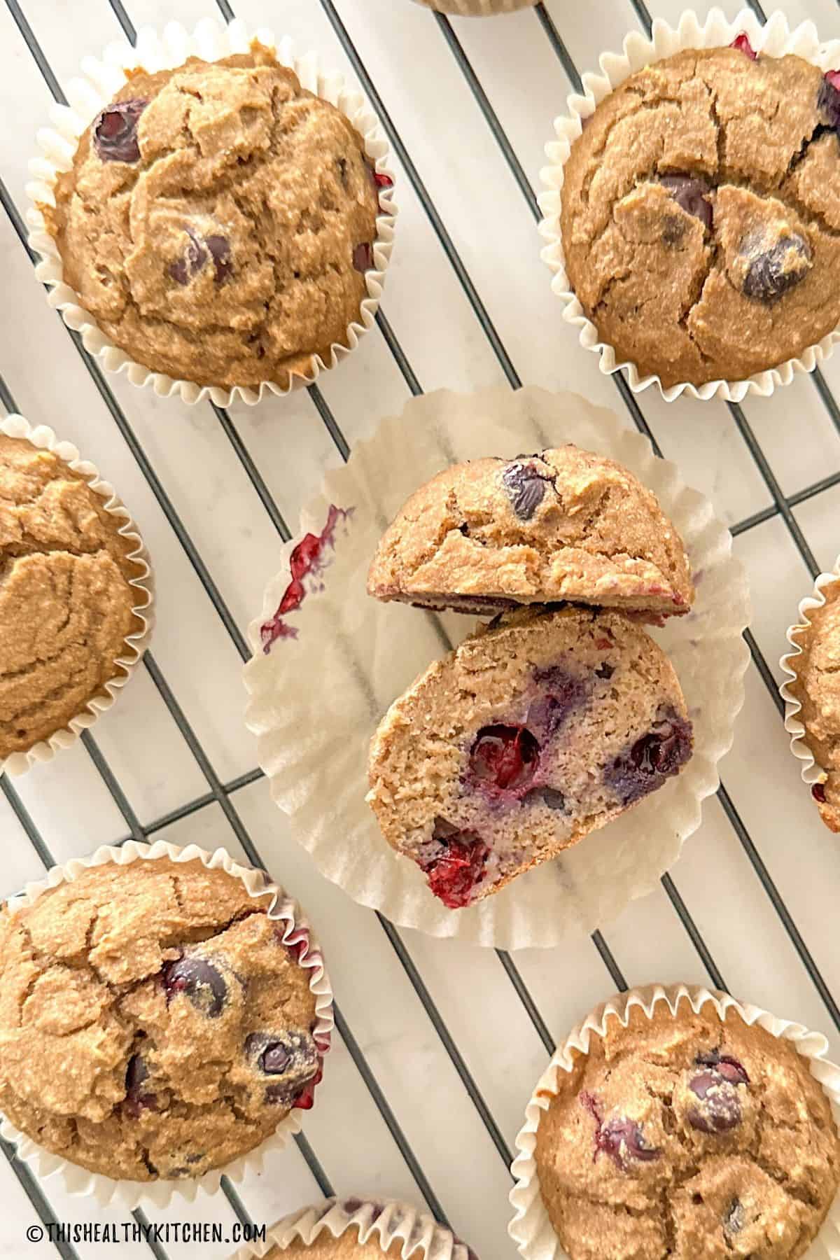 Muffin sliced in half on wire rack with more muffins all around it.