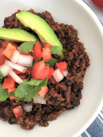 Rice and beans in bowl with onion, tomato, cilantro, and avocado on top.