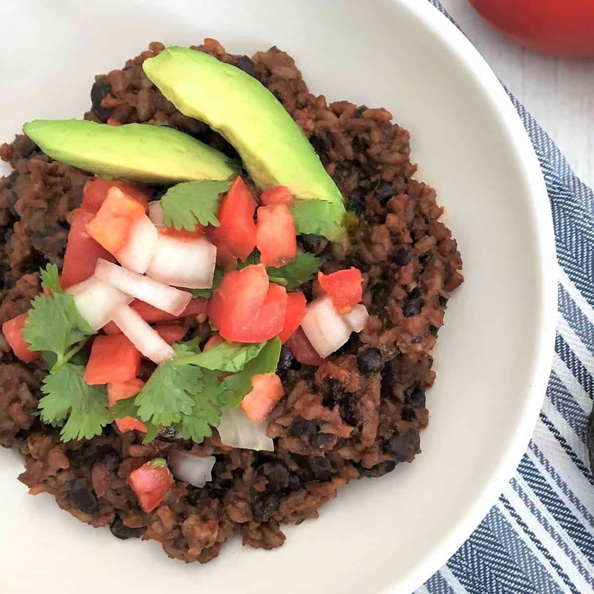 Rice and beans in bowl with onion, tomato, cilantro, and avocado on top.