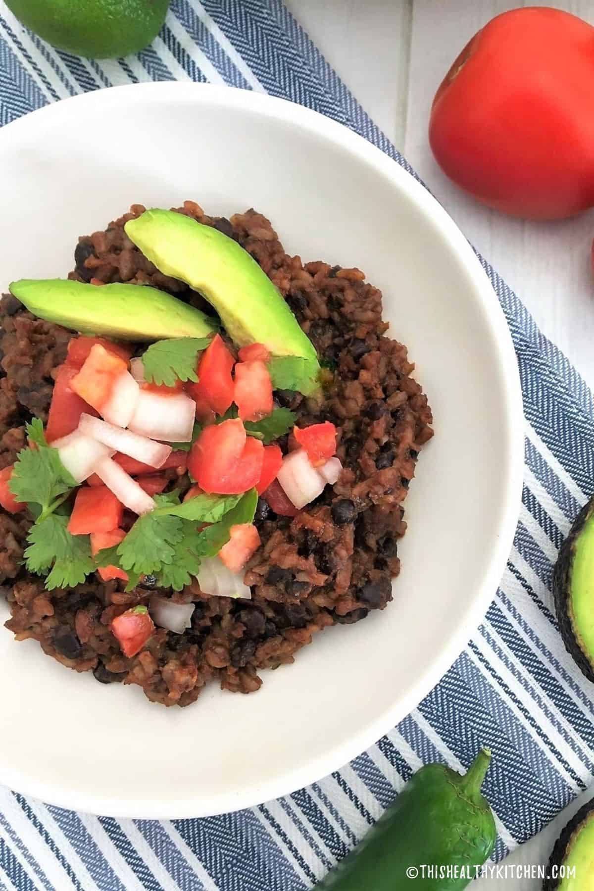 Instant Pot rice and beans inside white dish with tomato, onion and avocado on top.