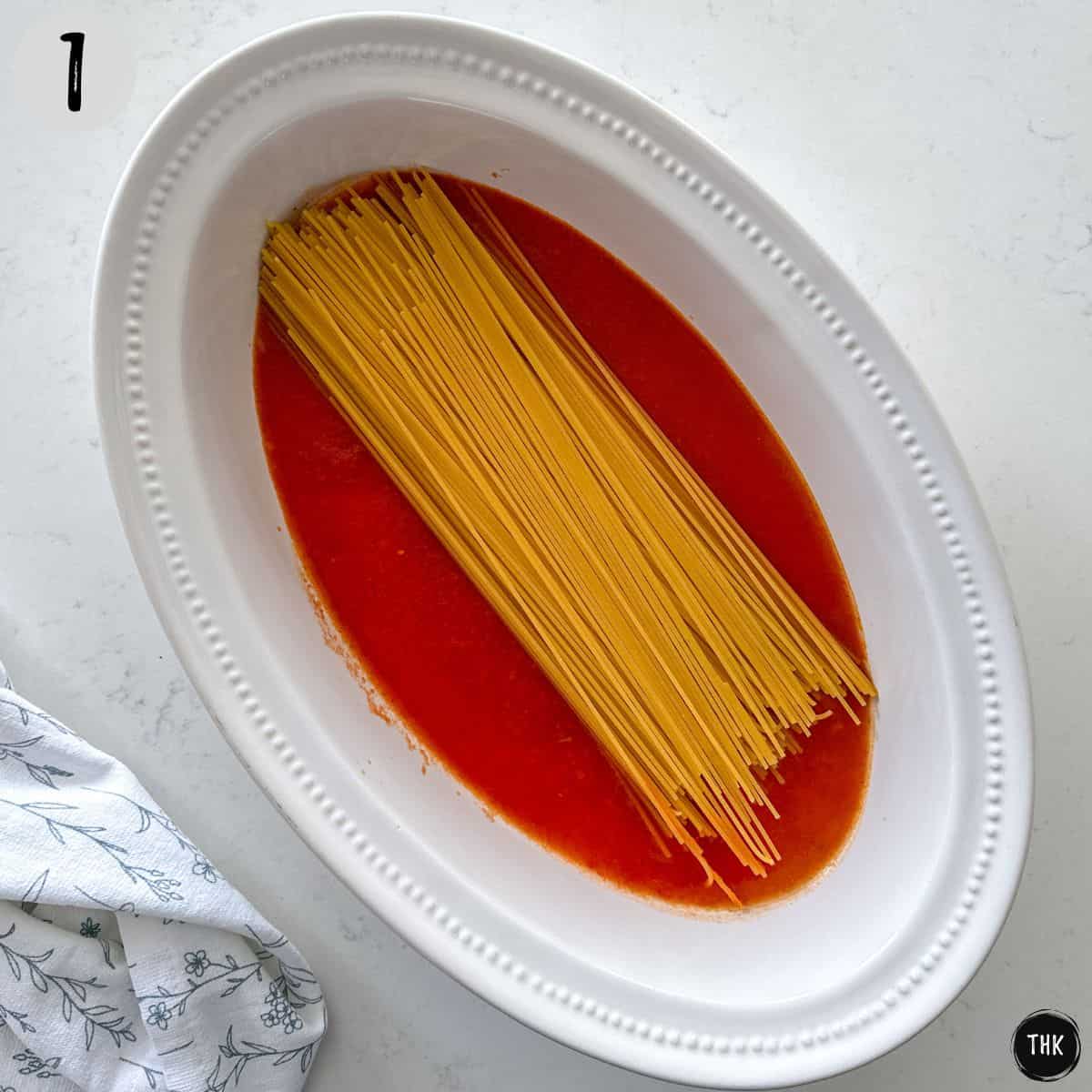 Casserole dish with tomato sauce and raw spaghetti on top.