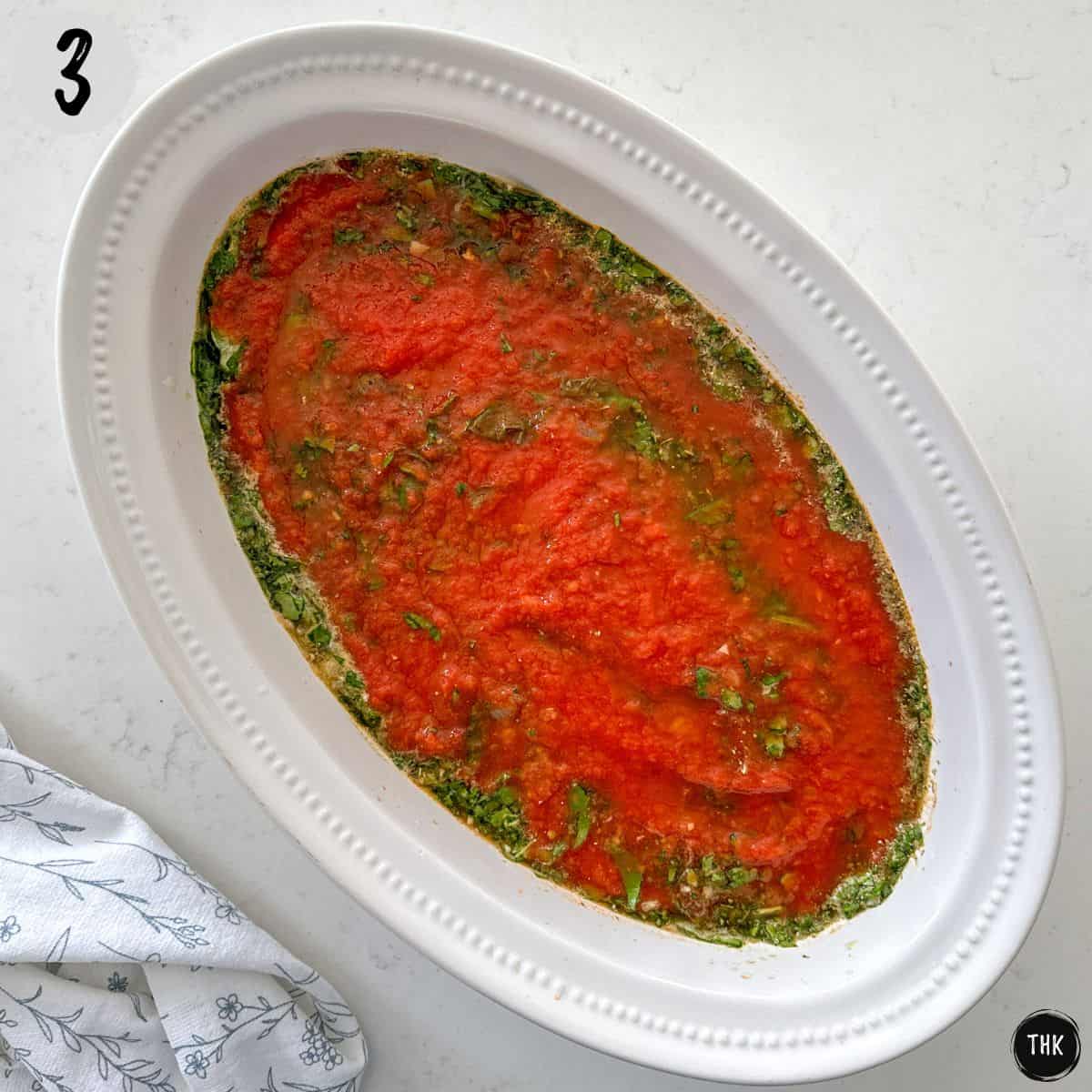 Casserole dish with broth, tomato sauce, and spinach inside.