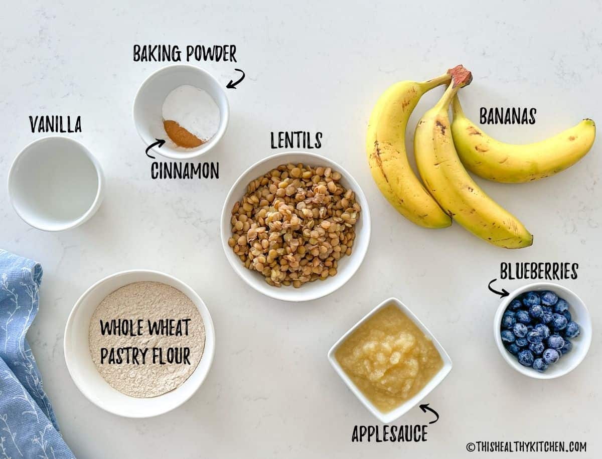Banana, lentils, flour, applesauce, blueberries, vanilla and baking powder on countertop.