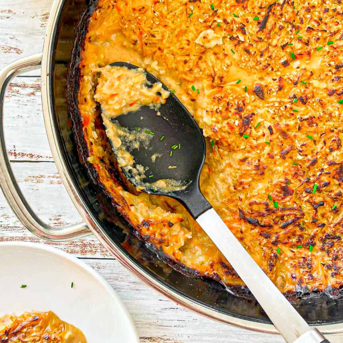 Vegan hash brown casserole in serving pan with serving spoon inside.