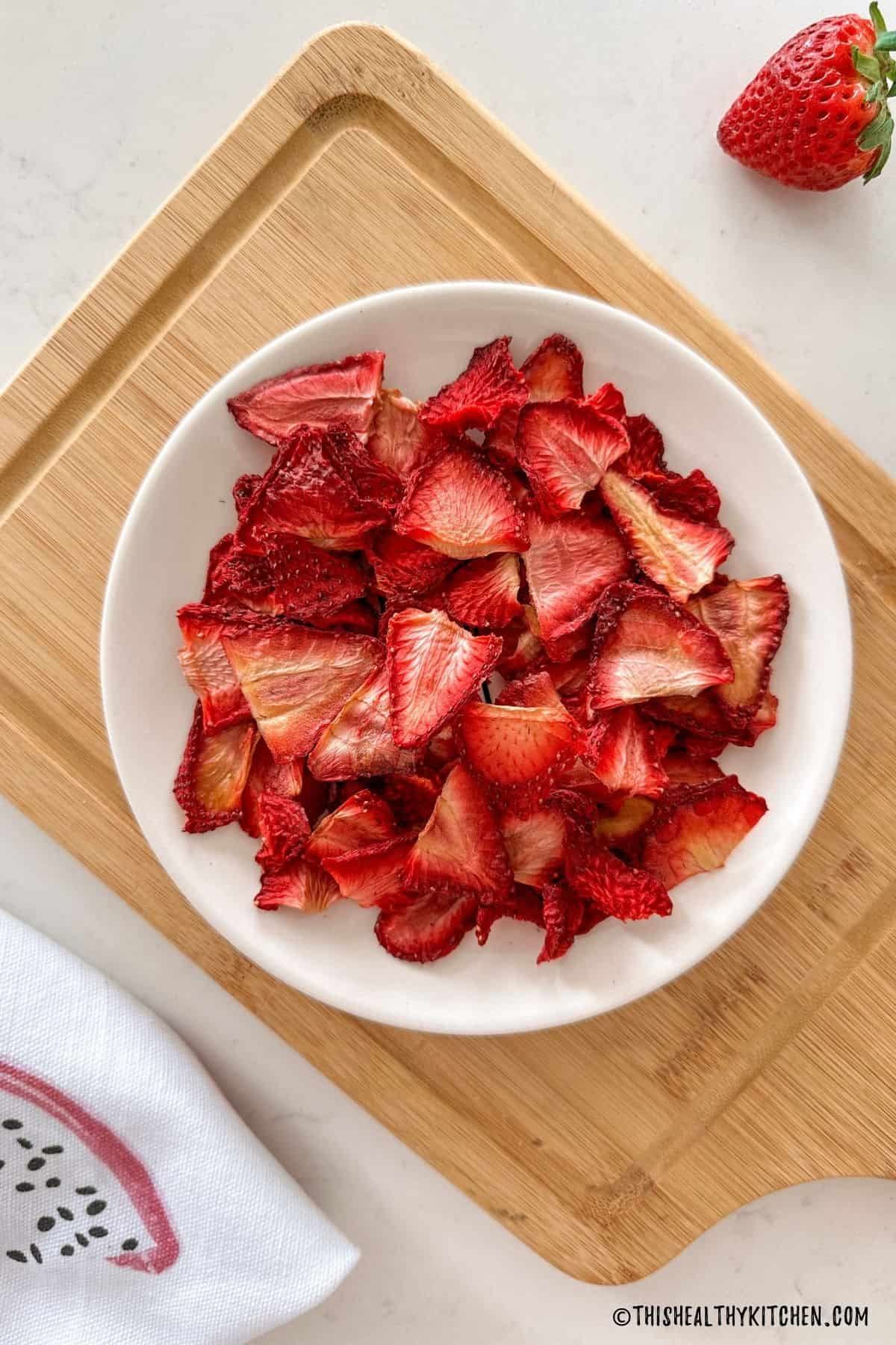 Air fryer strawberries in white plate sitting on cutting board.