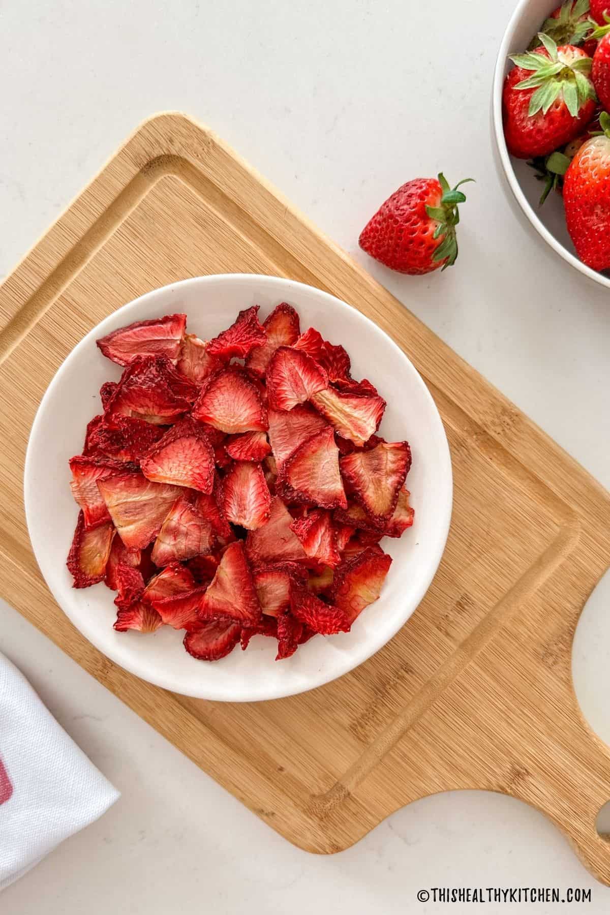 Dehydrated strawberries in white plate sitting on cutting board.