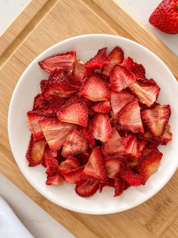 Air fryer strawberries in white plate sitting on cutting board.