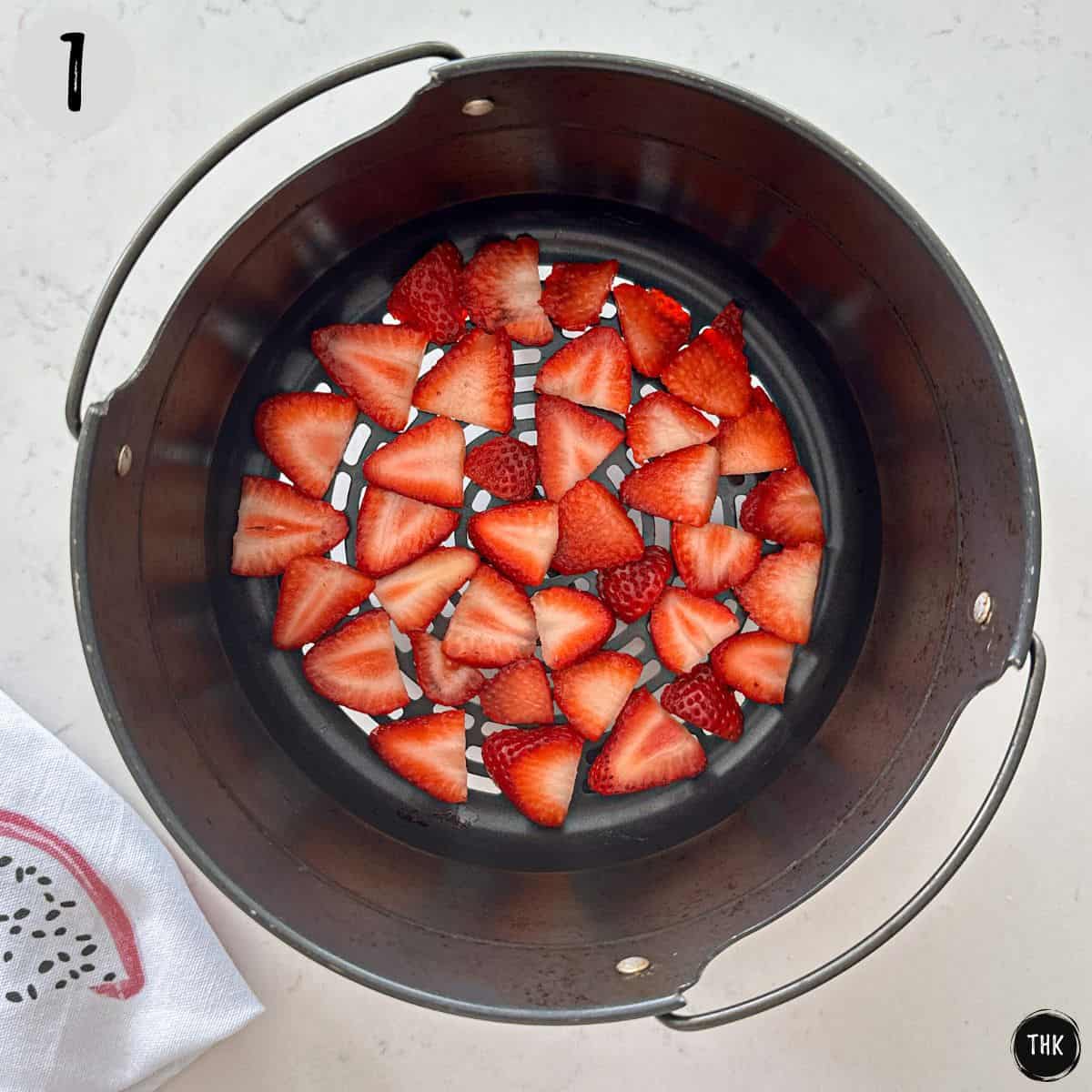 Slice strawberries inside air fryer basket.