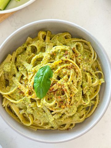 Bowl of fettuccini with pesto sauce, red pepper flakes and basil on top.