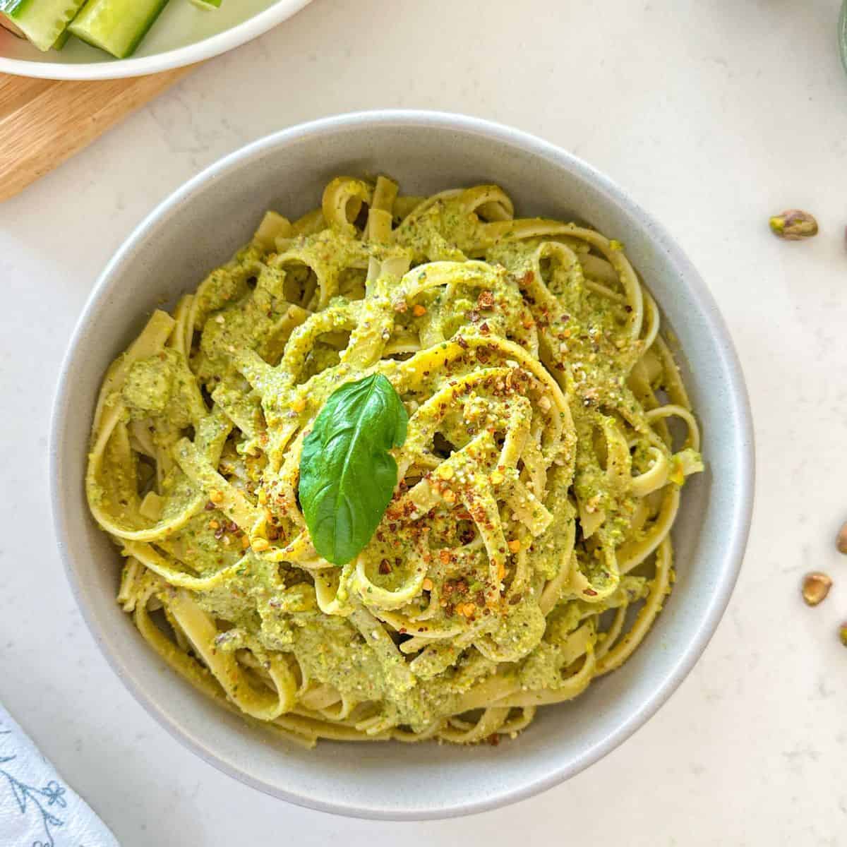 Bowl of fettuccini with pesto sauce, red pepper flakes and basil on top.
