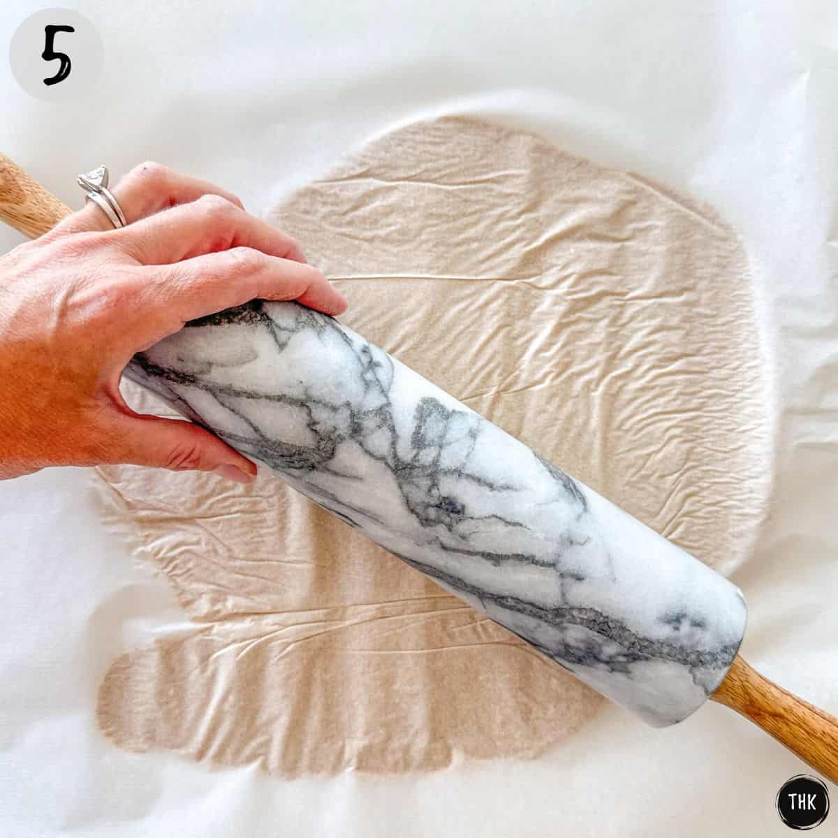 Rolling pin stretching out dough in between sheets of parchment paper.