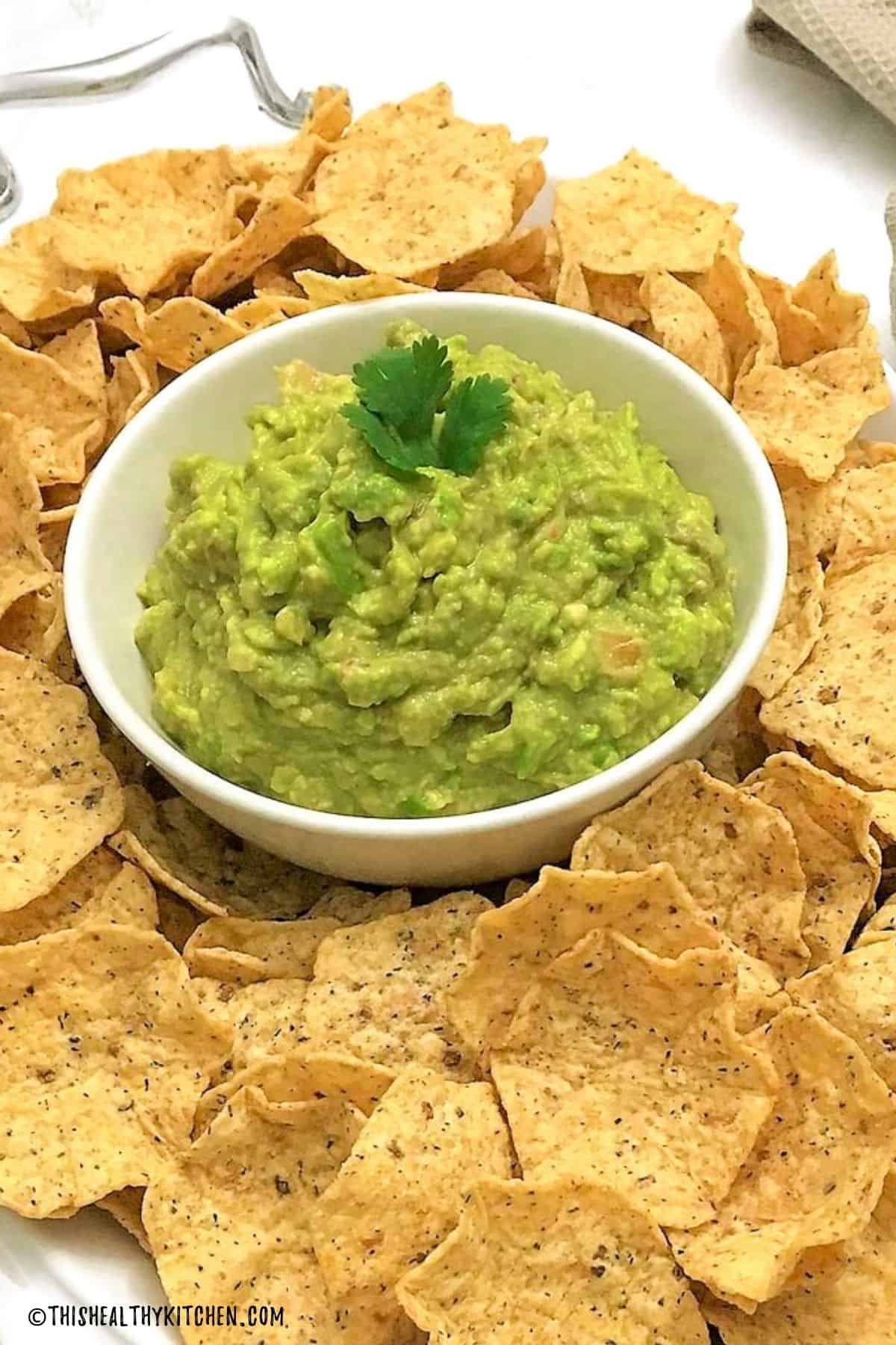 Platter of tortilla chips with bowl of guacamole in the middle.