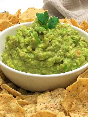 Bowl of guacamole with tortilla chips all around it.