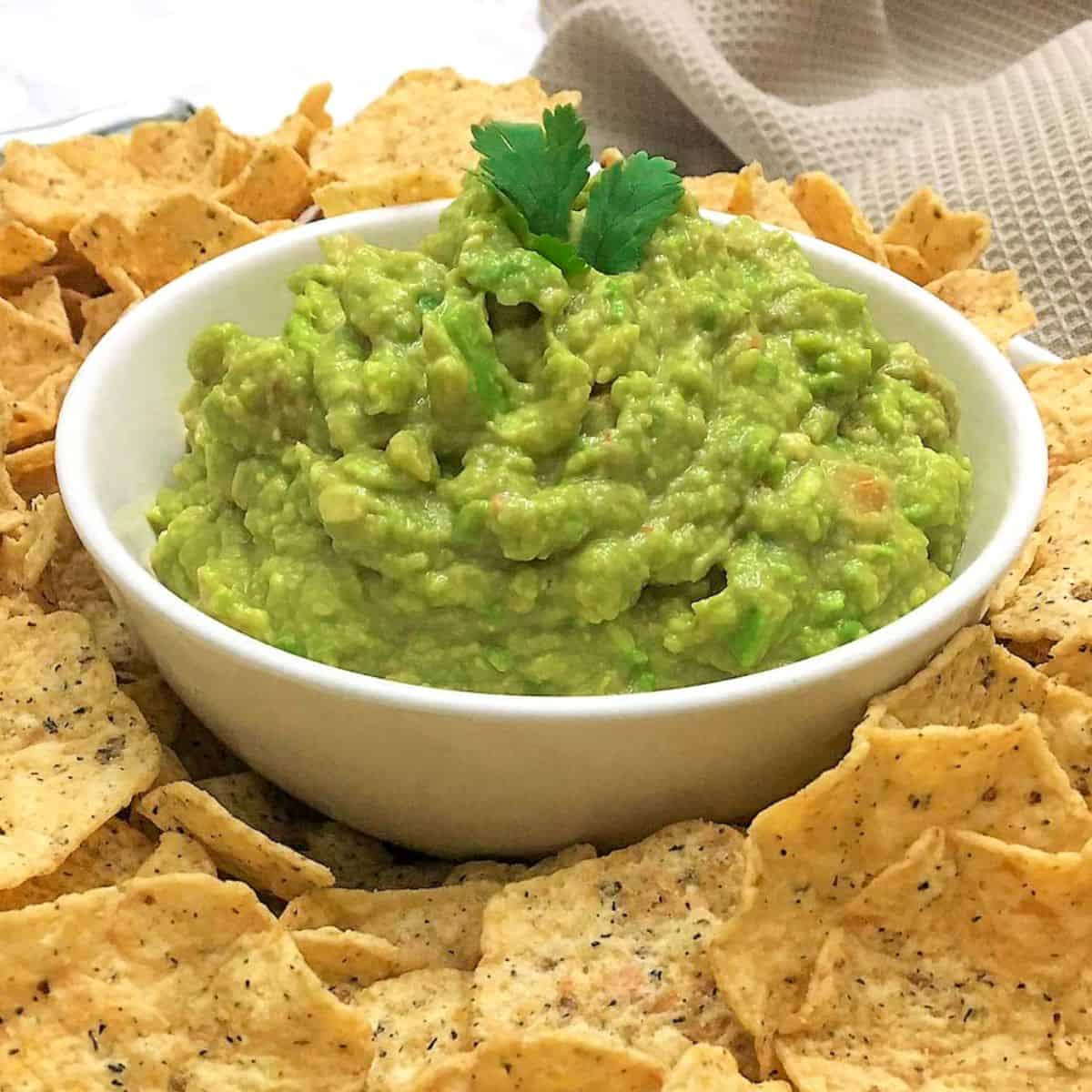 Bowl of guacamole with tortilla chips all around it.