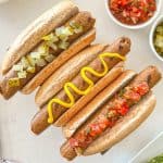 Three tofu hot dogs in buns with toppings.