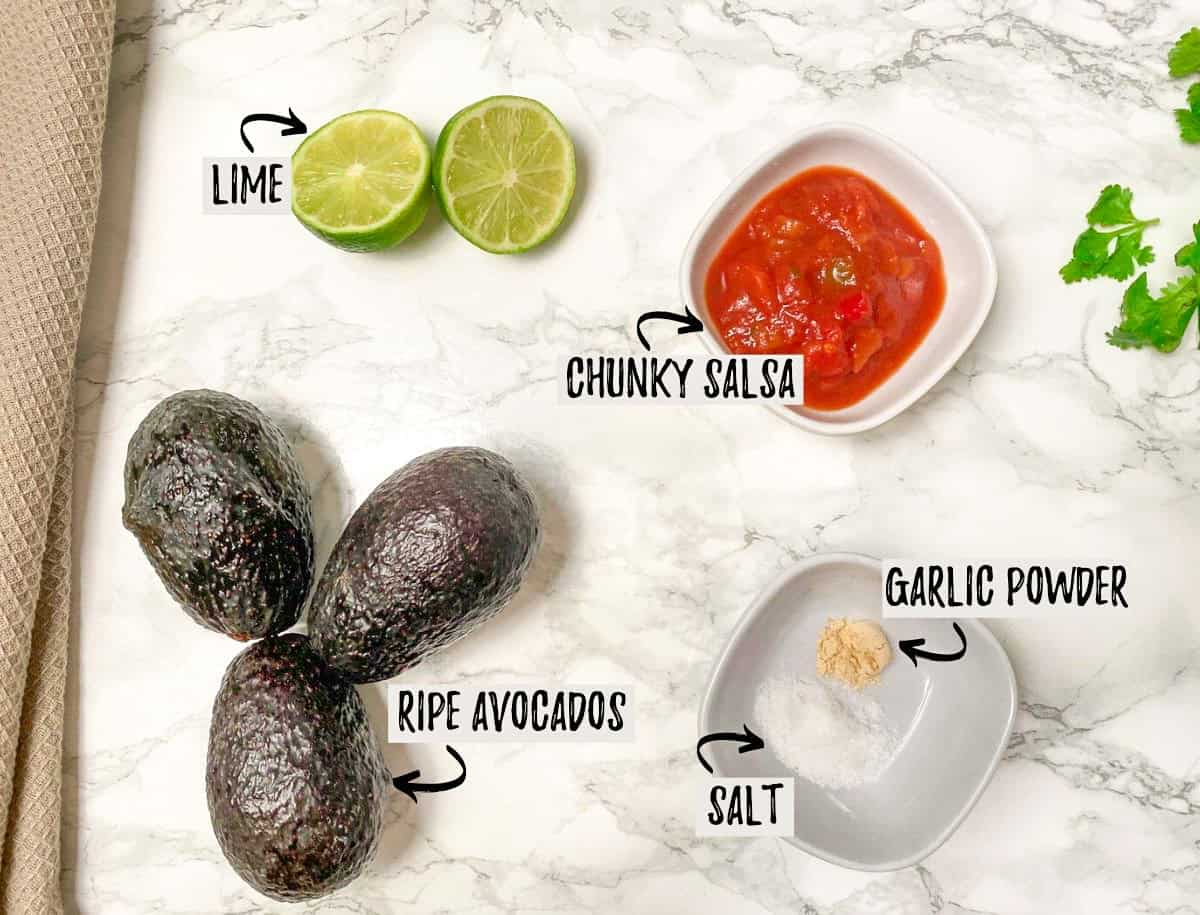 Avocados, lime, salsa, and spices on kitchen countertop.