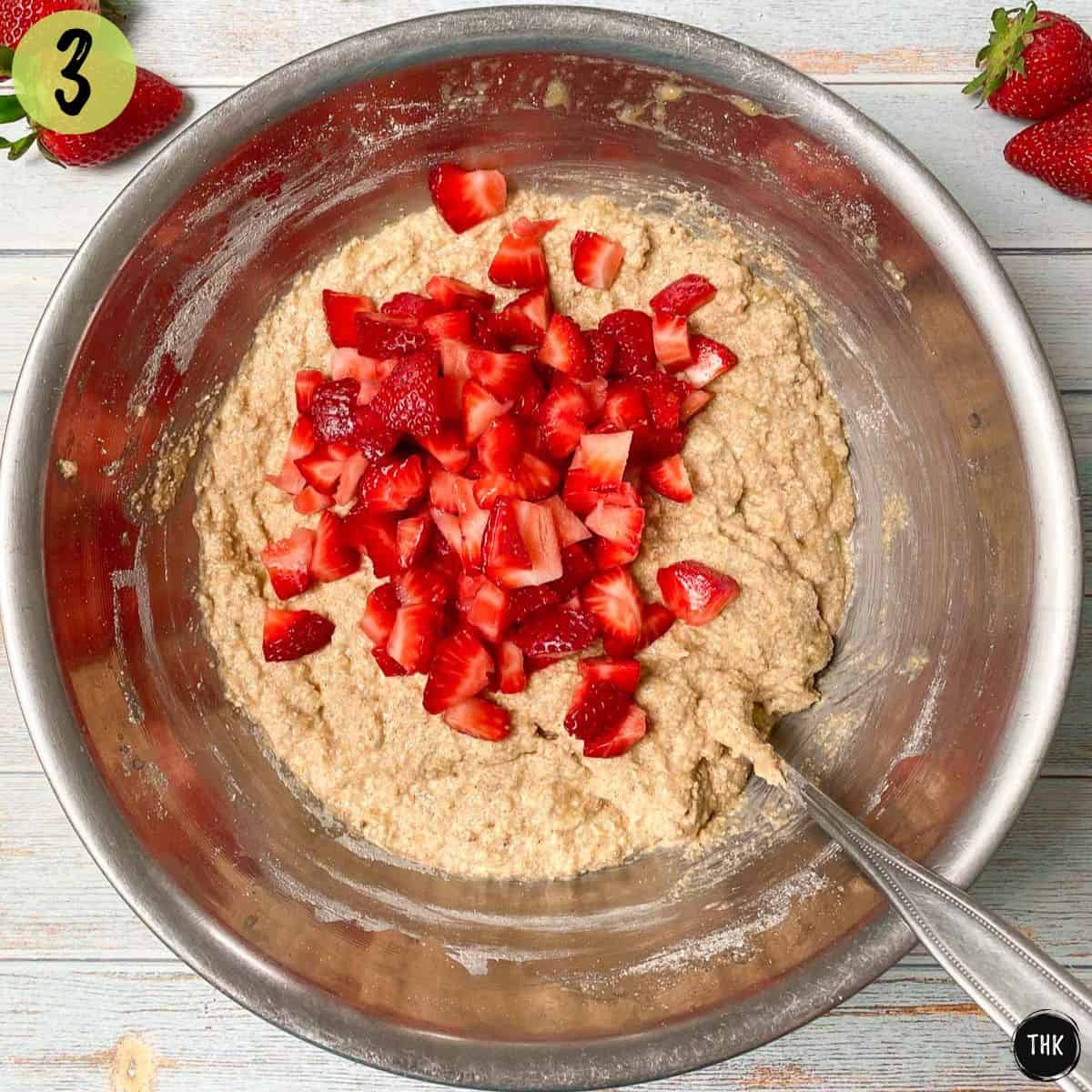 Banana bread batter with diced strawberries on top in mixing bowl.