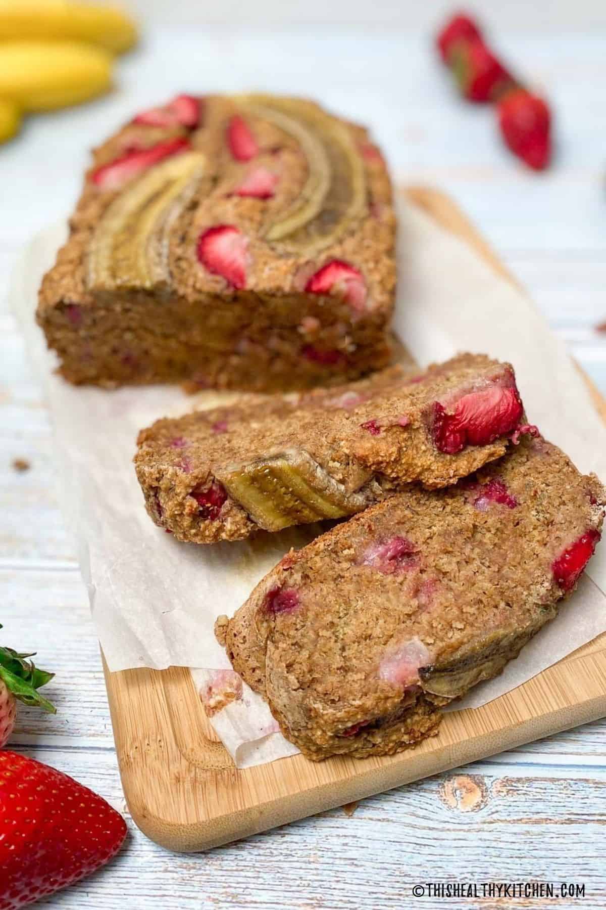 Banana strawberry bread on cutting board with two slices made.