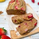Banana strawberry bread on cutting board with two slices made and strawberries beside it.