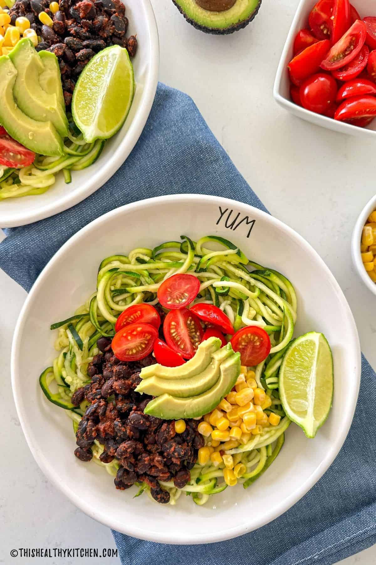 Zucchini noodle bowl with avocado, tomato, black beans and a lime wedge on top.