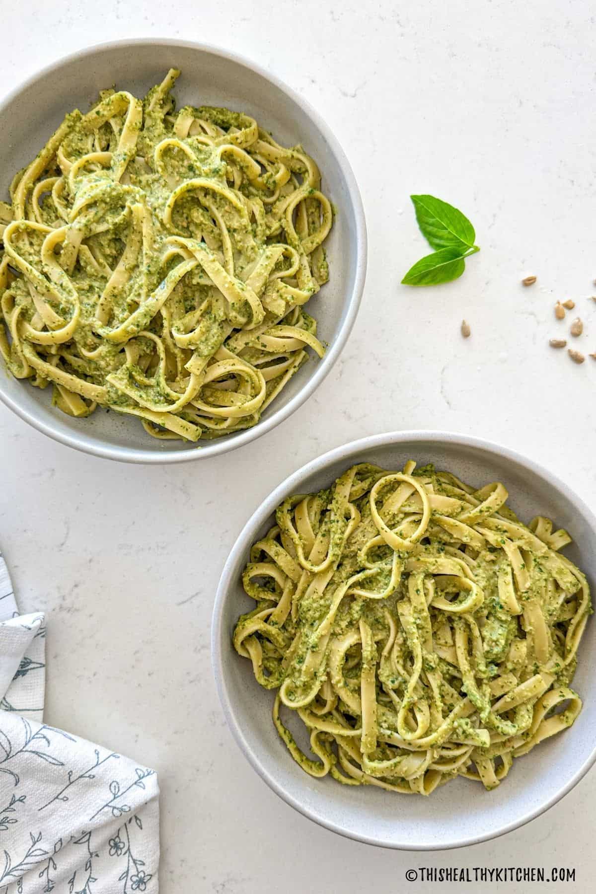 Two bowls of miso pesto pasta with basil and sunflower seeds on the side.
