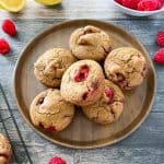 Raspberry muffins in brown bamboo plate with raspberries scattered around it.