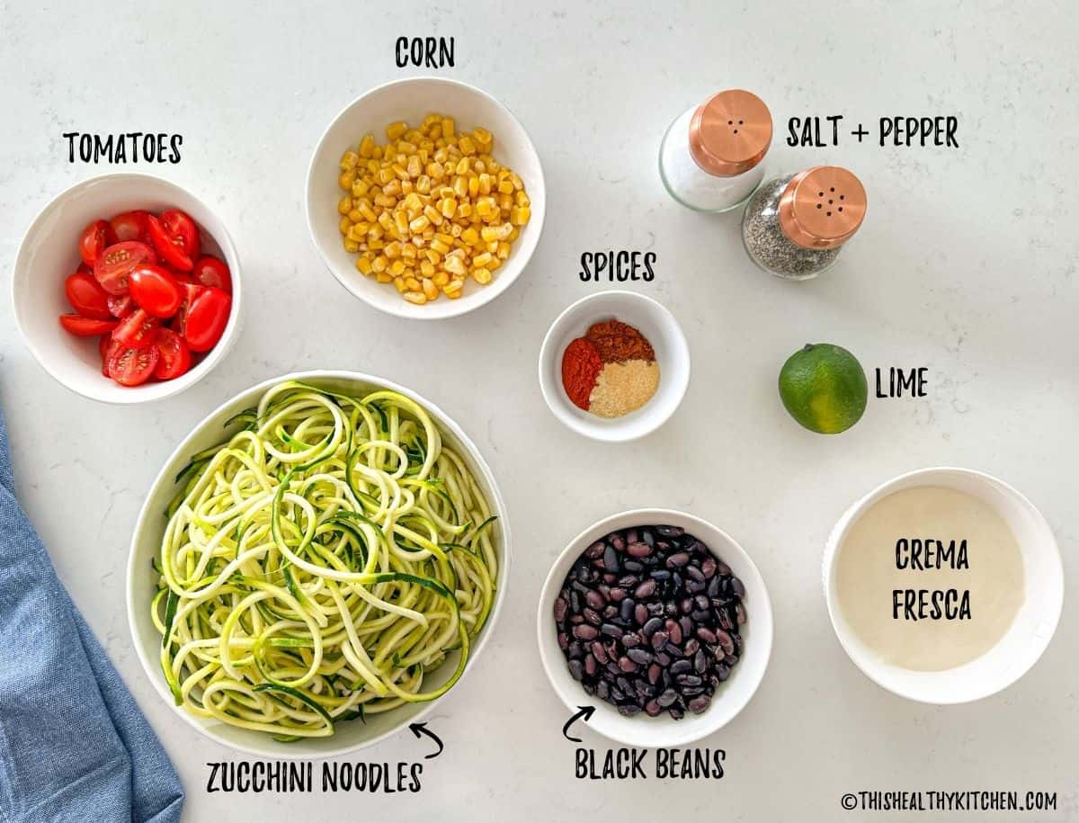 Bowls of zucchini noodles, corn, tomatoes, spices, beans, and lime.