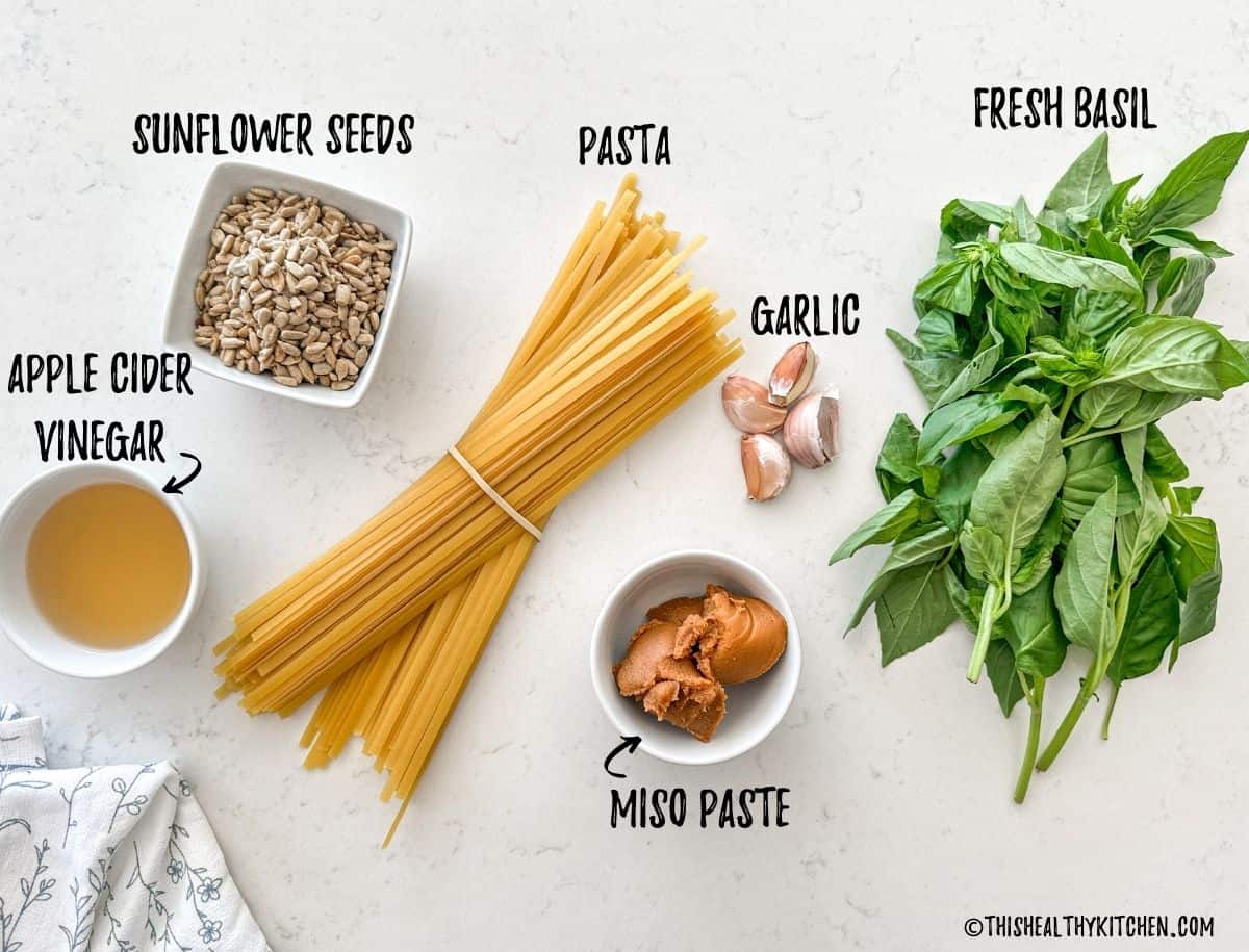 Fettuccini, sunflower seeds, apple cider vinegar, miso pasta, garlic and basil on kitchen countertop.