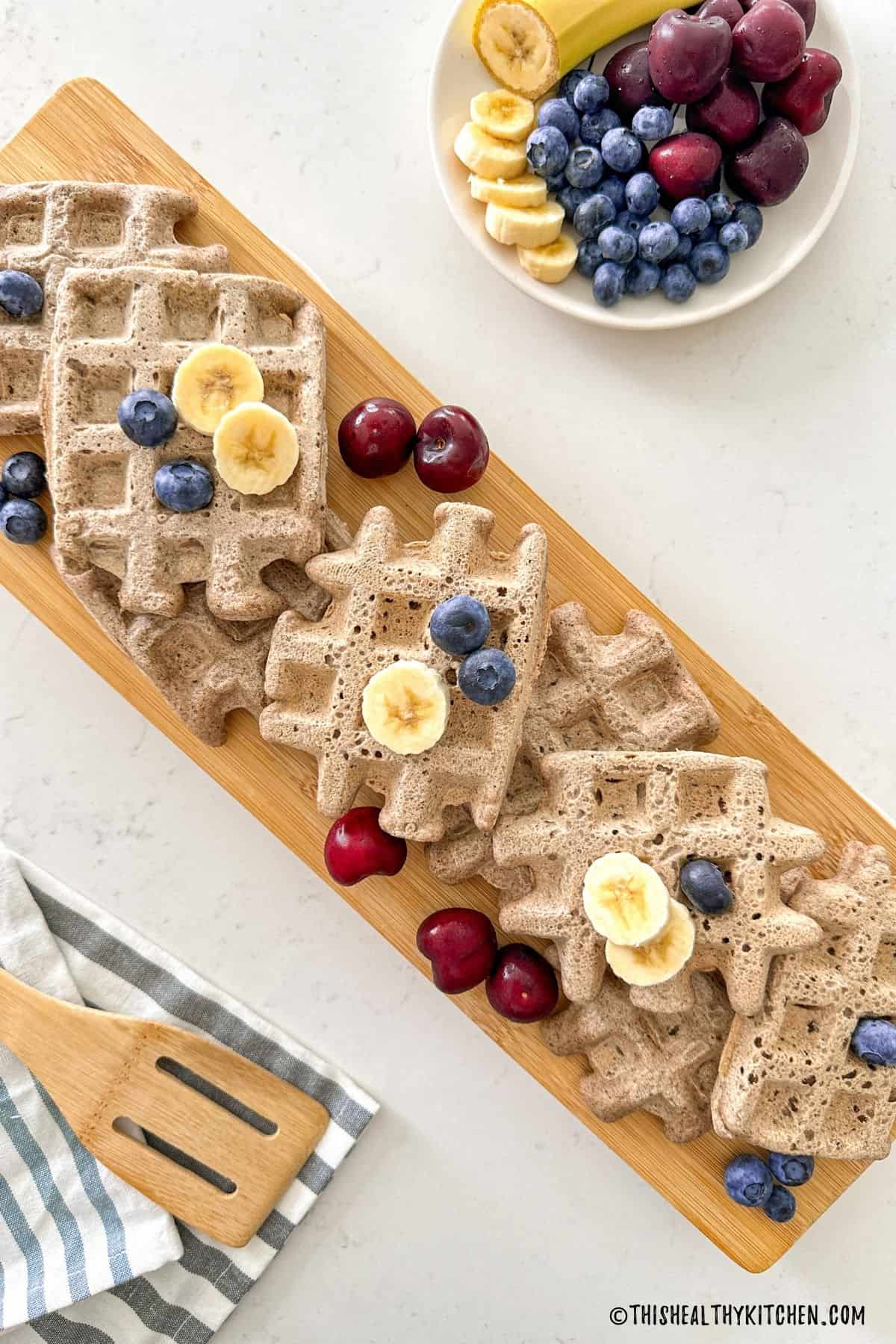 Buckwheat waffles on cutting board with blueberries, cherries and banana slices on top.