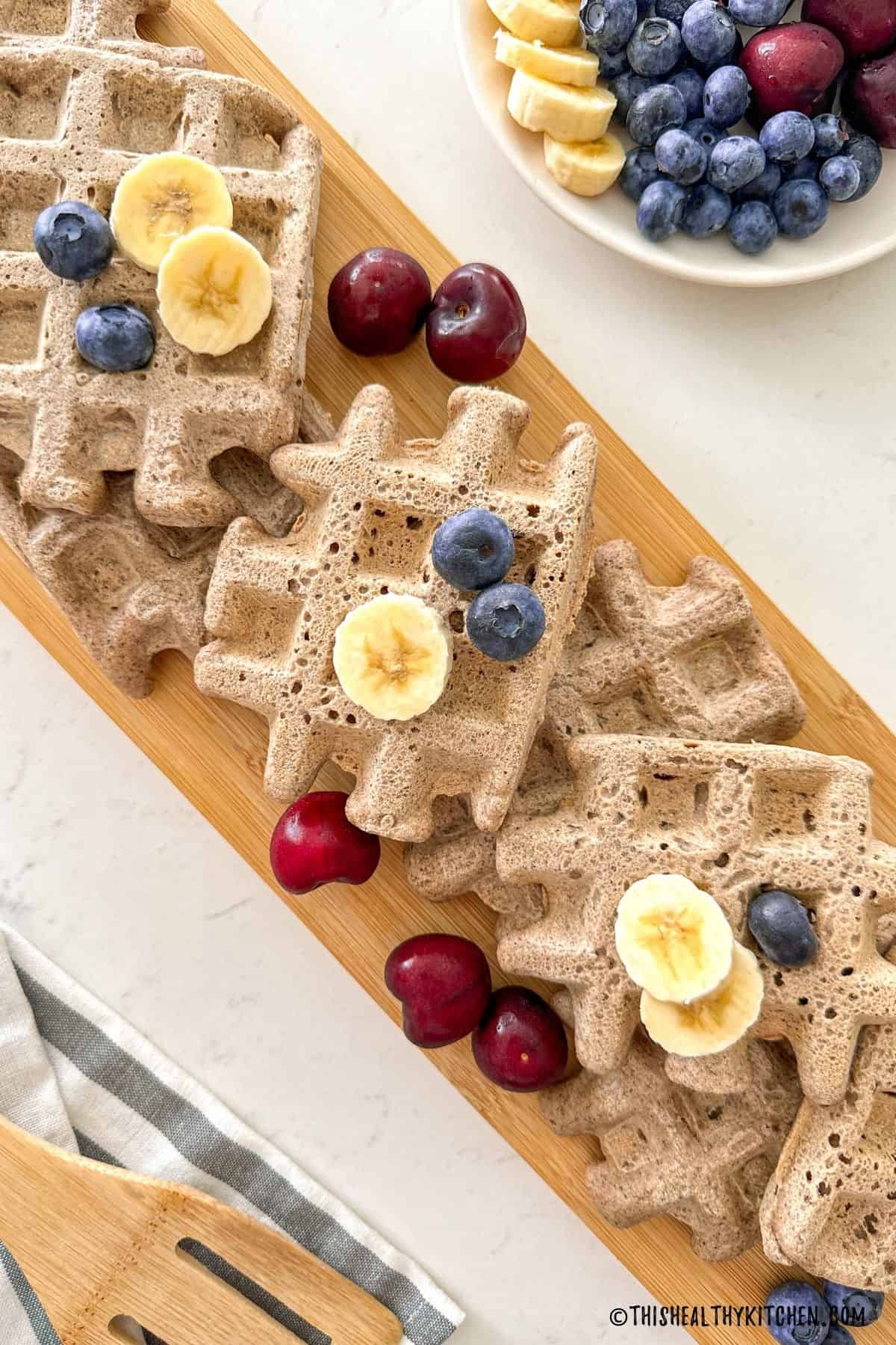 Buckwheat waffles on cutting board with blueberries, cherries and banana slices on top.