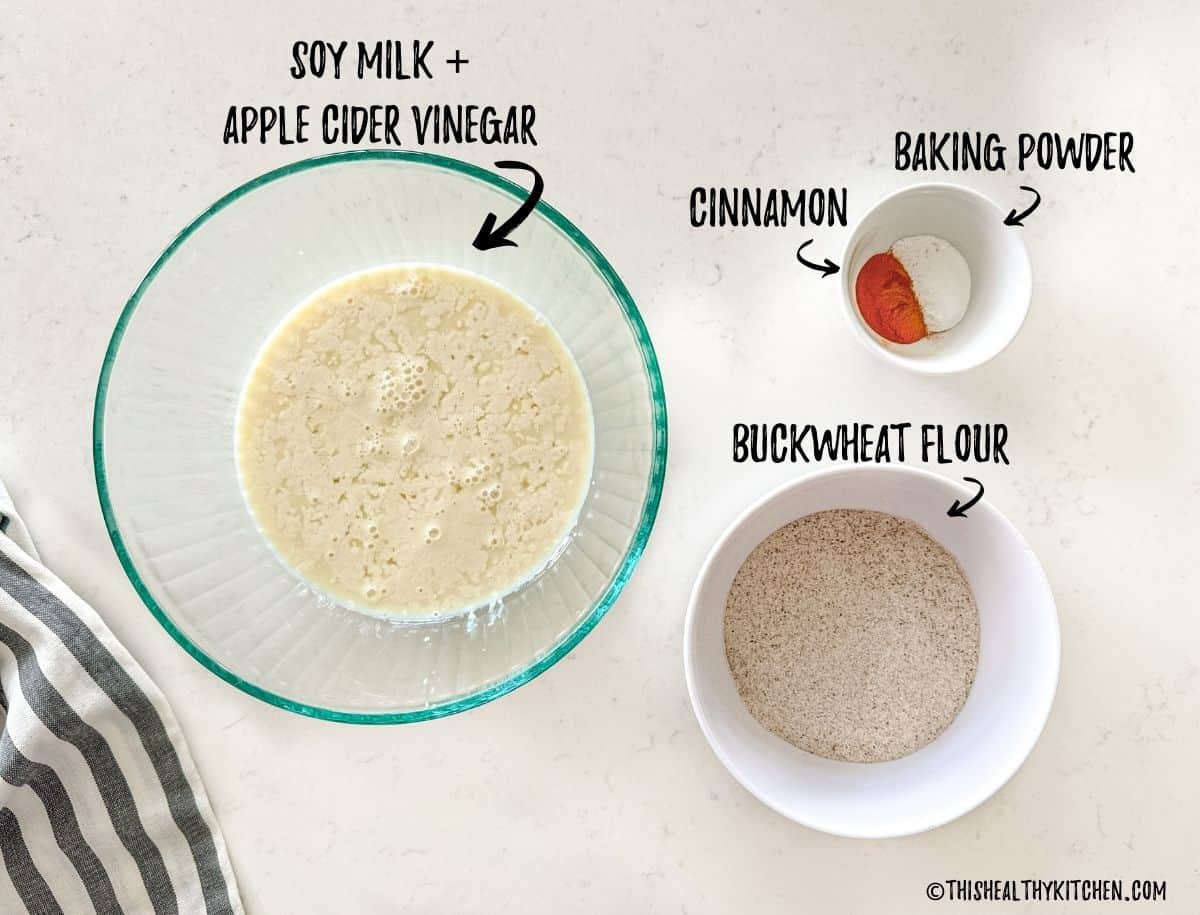 Bowl of curdled milk, bowl of flour, and bowl with cinnamon and baking powder on countertop.