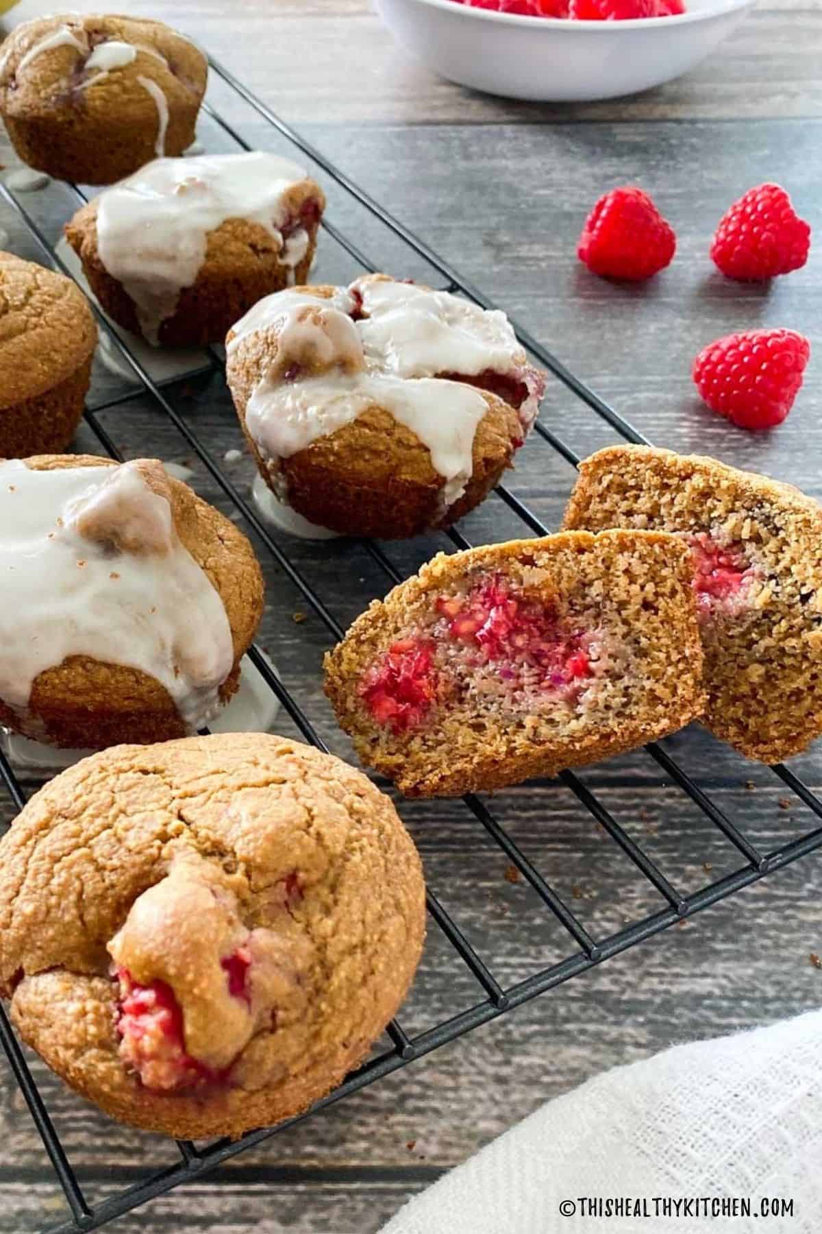 Raspberry muffins on cooling rack with one sliced in half to expose fruit inside.