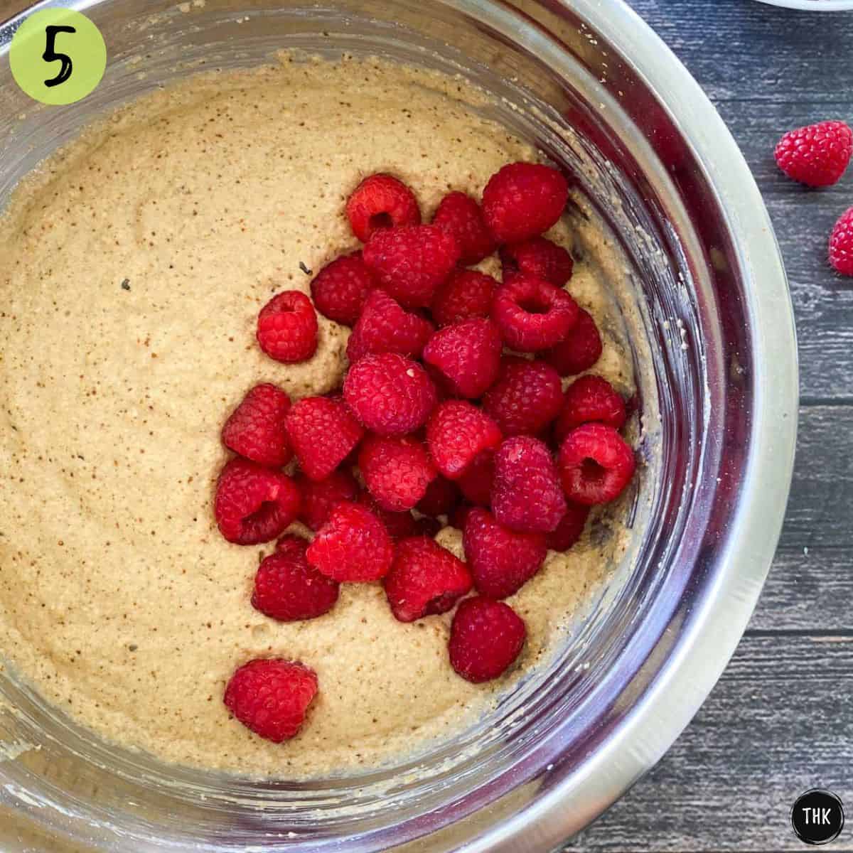 Muffin batter inside large mixing bowl with raspberries on top.