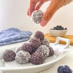 White plate of bliss balls with blueberries in the background.