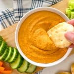 Pita bread being dipped into bowl of orange lentil dip.
