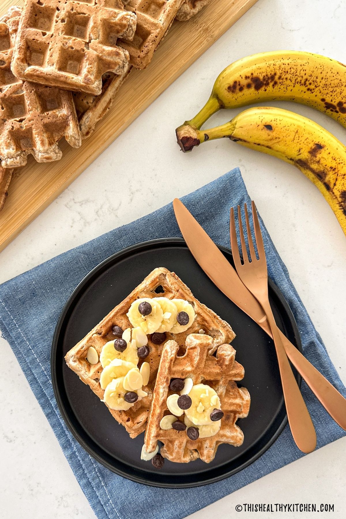 Waffles on cutting board and two on a plate with banana slices and chocolate chips on top.