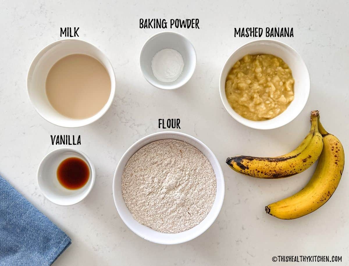 Bowls of mashed banana, milk, baking powder, vanilla and flour on kitchen countertop.