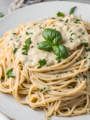Plate of spaghetti with vegan alfredo sauce and fresh basil on top.