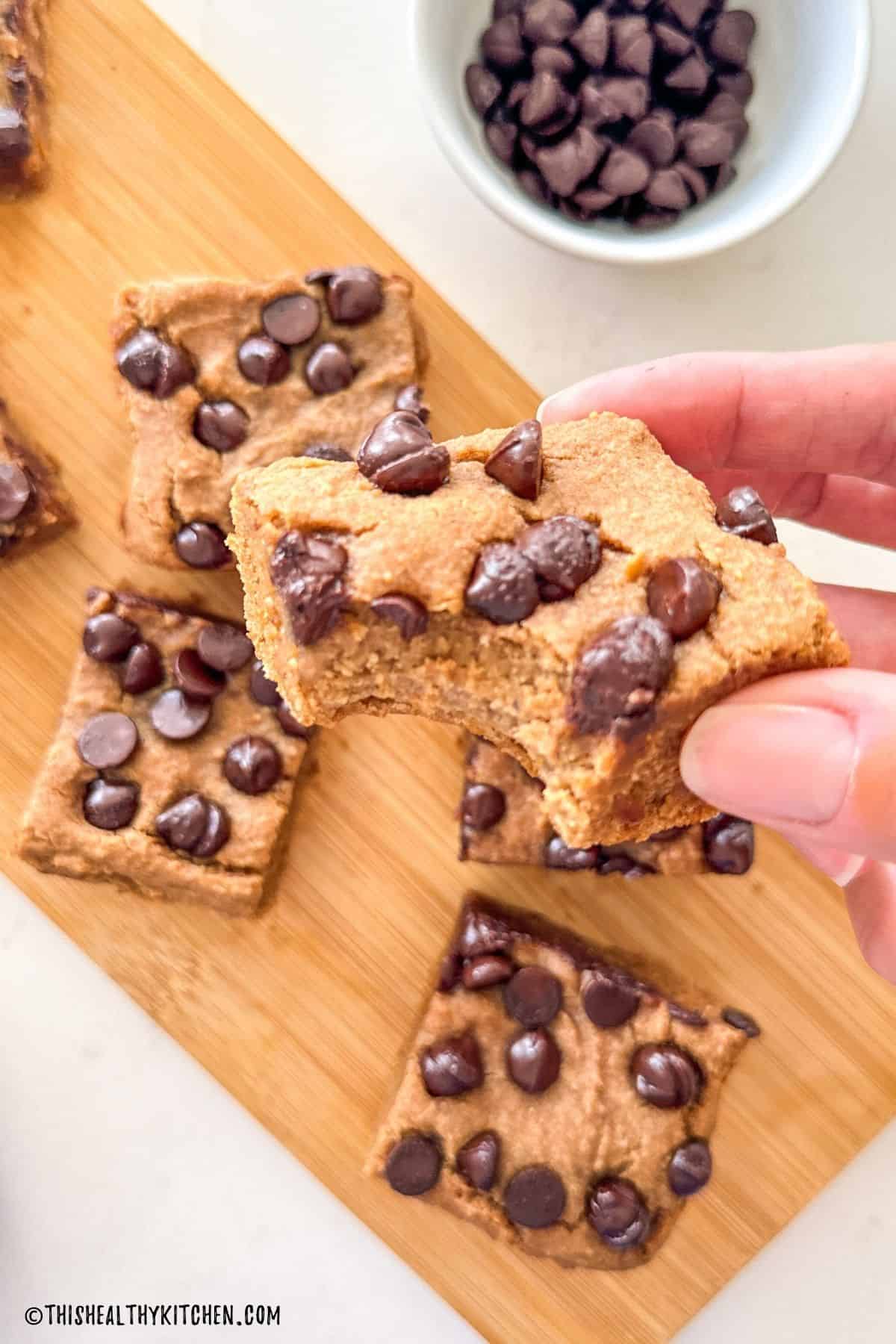 Hand holding up a white bean blondie with a bite taken from it.