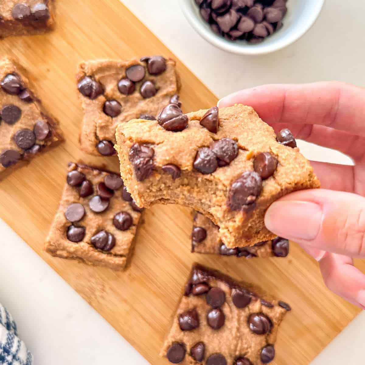 Hand holding up a white bean blondie with a bite taken from it.