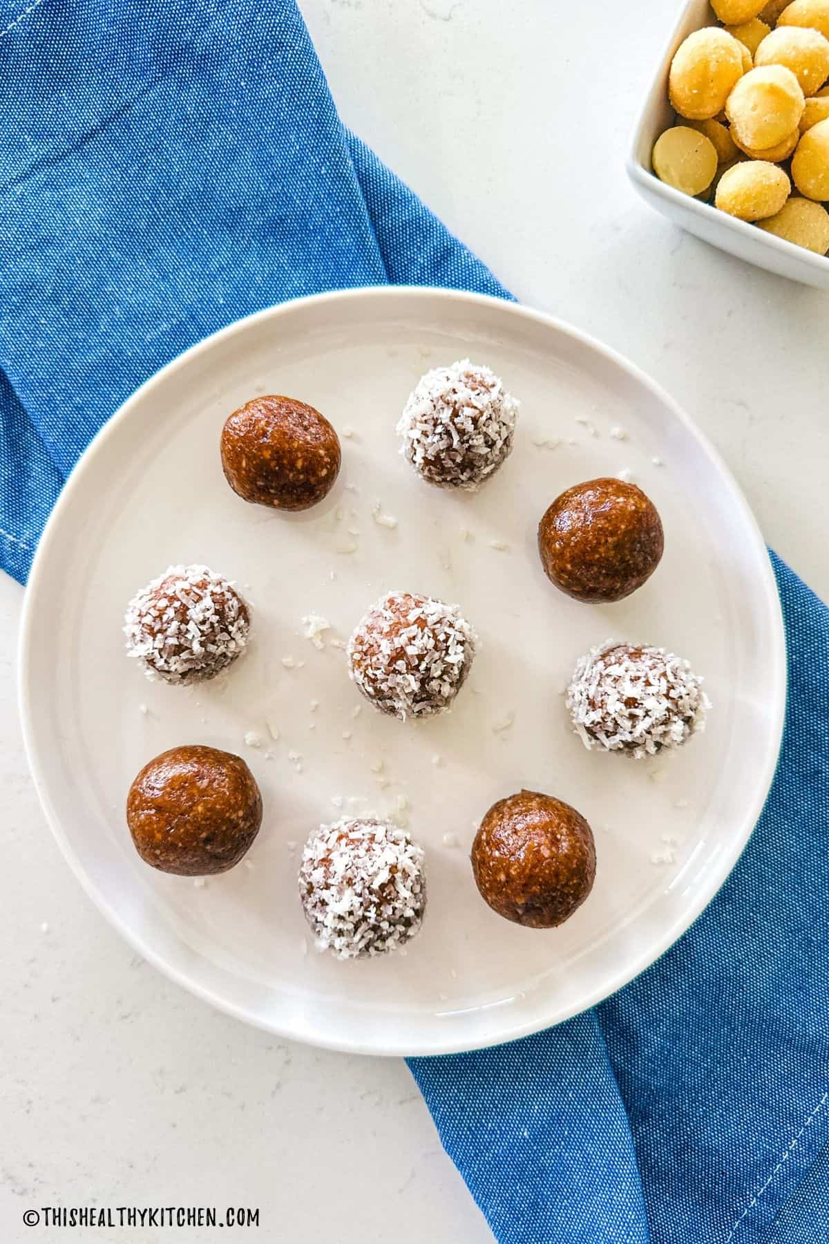 Salted caramel bliss balls on white plate with blue kitchen towel underneath.
