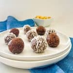 Bliss balls on white plate with bowl of macadamia nuts in the background.