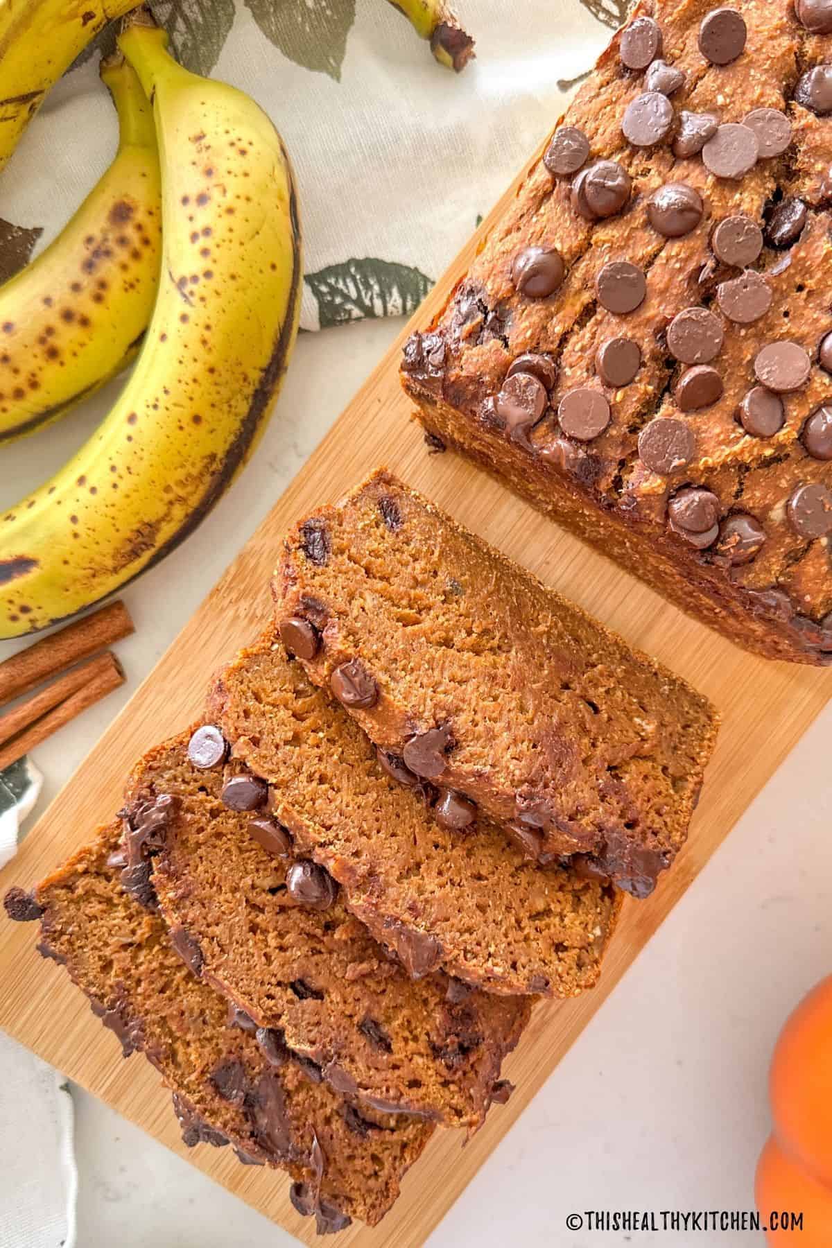 Pumpkin banana bread with chocolate chips on wooden cutting board.