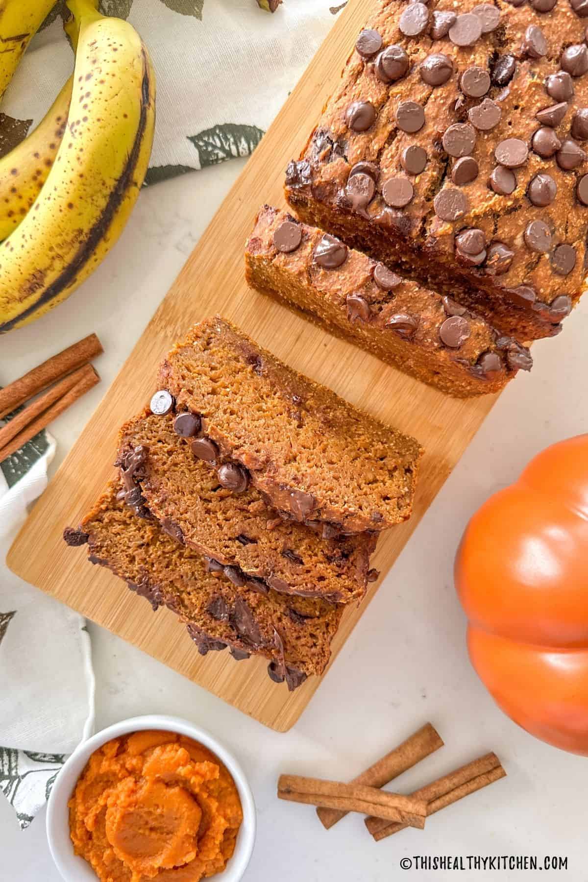 Sliced banana pumpkin bread on cutting board with cinnamon sticks around it.
