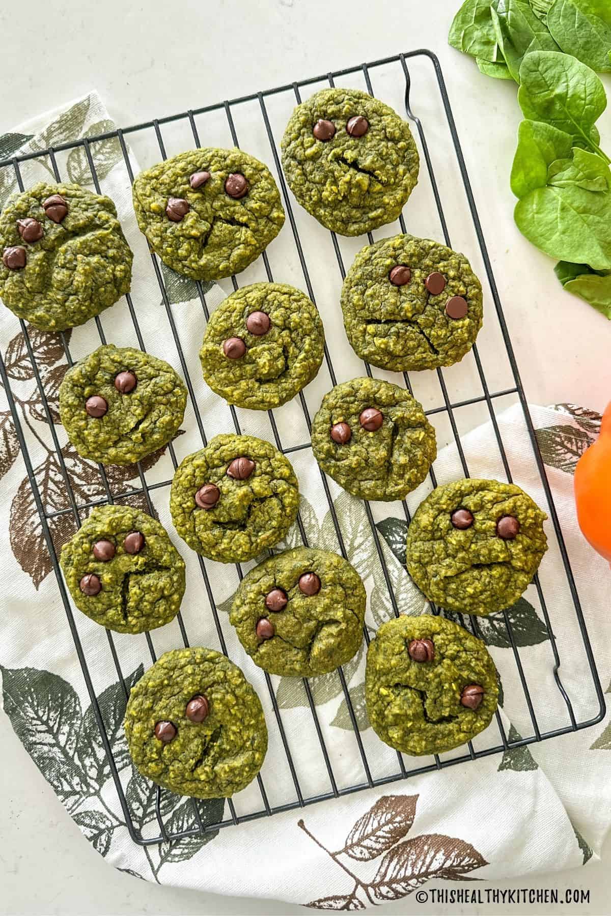 Green halloween cookies with chocolate chip eyes on cooling rack.