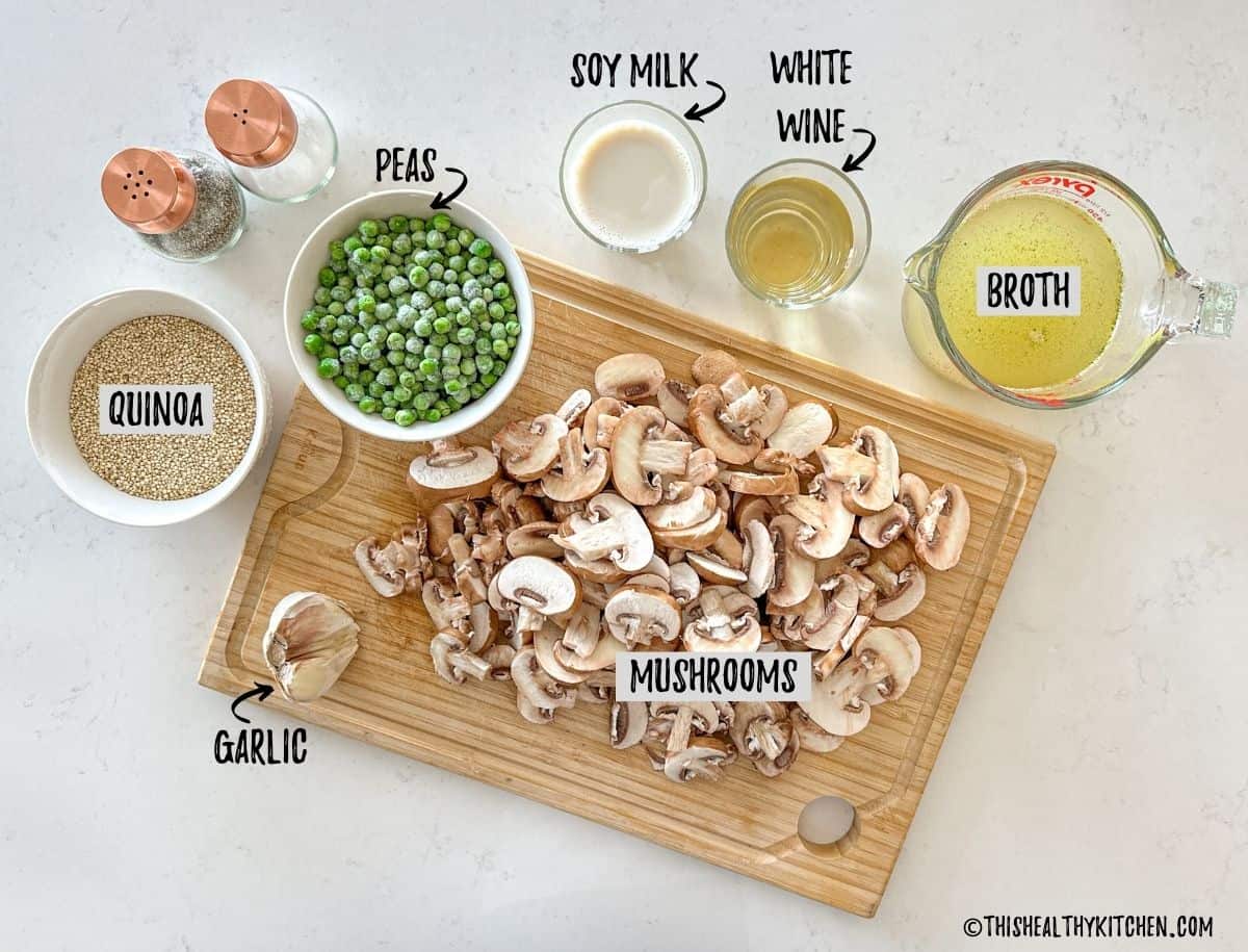 Cutting board with sliced mushrooms on top, with bowls of peas, broth, quinoa and white wine around it.