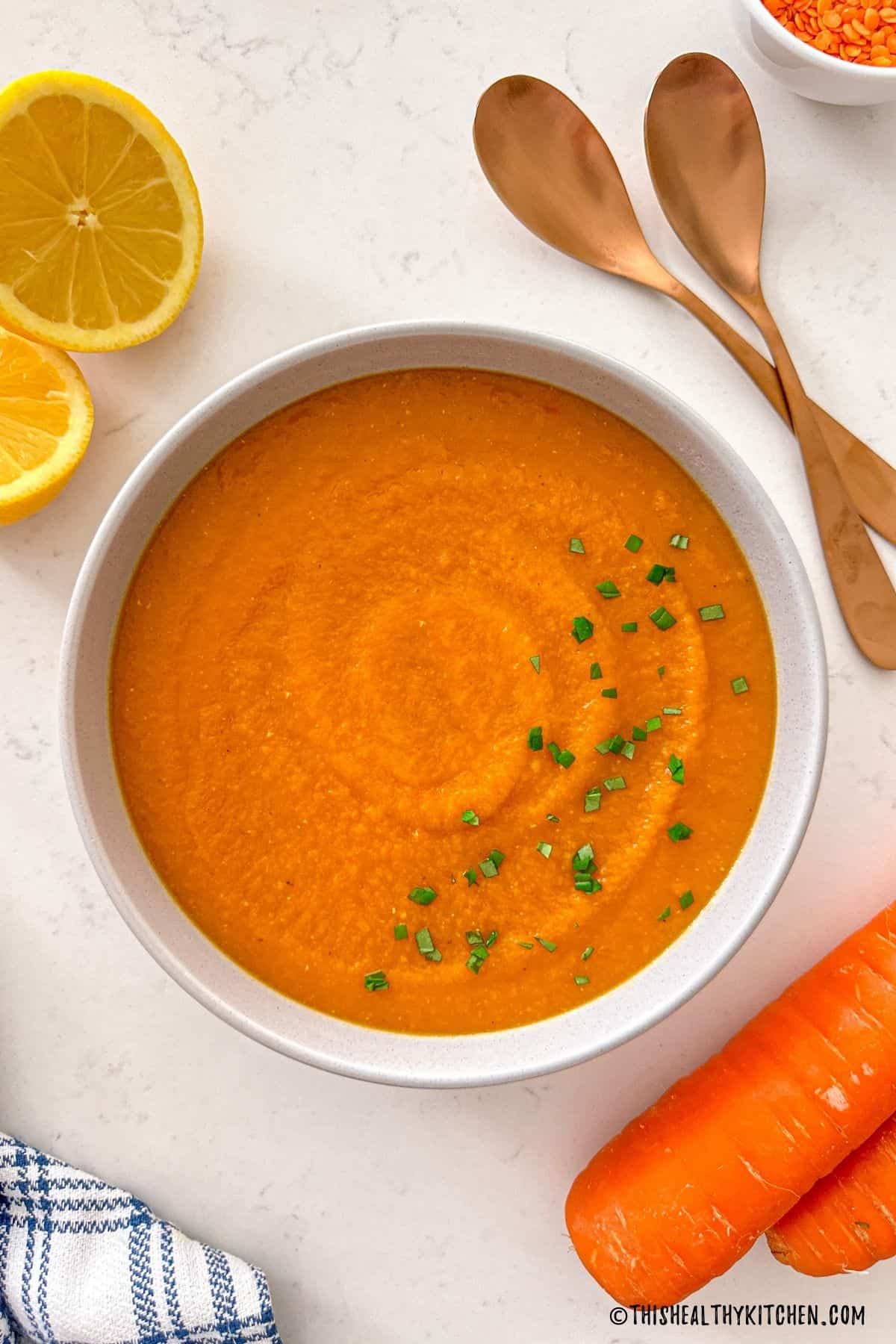 Bowl of orange creamy soup with green garnish on top and carrots on the side.