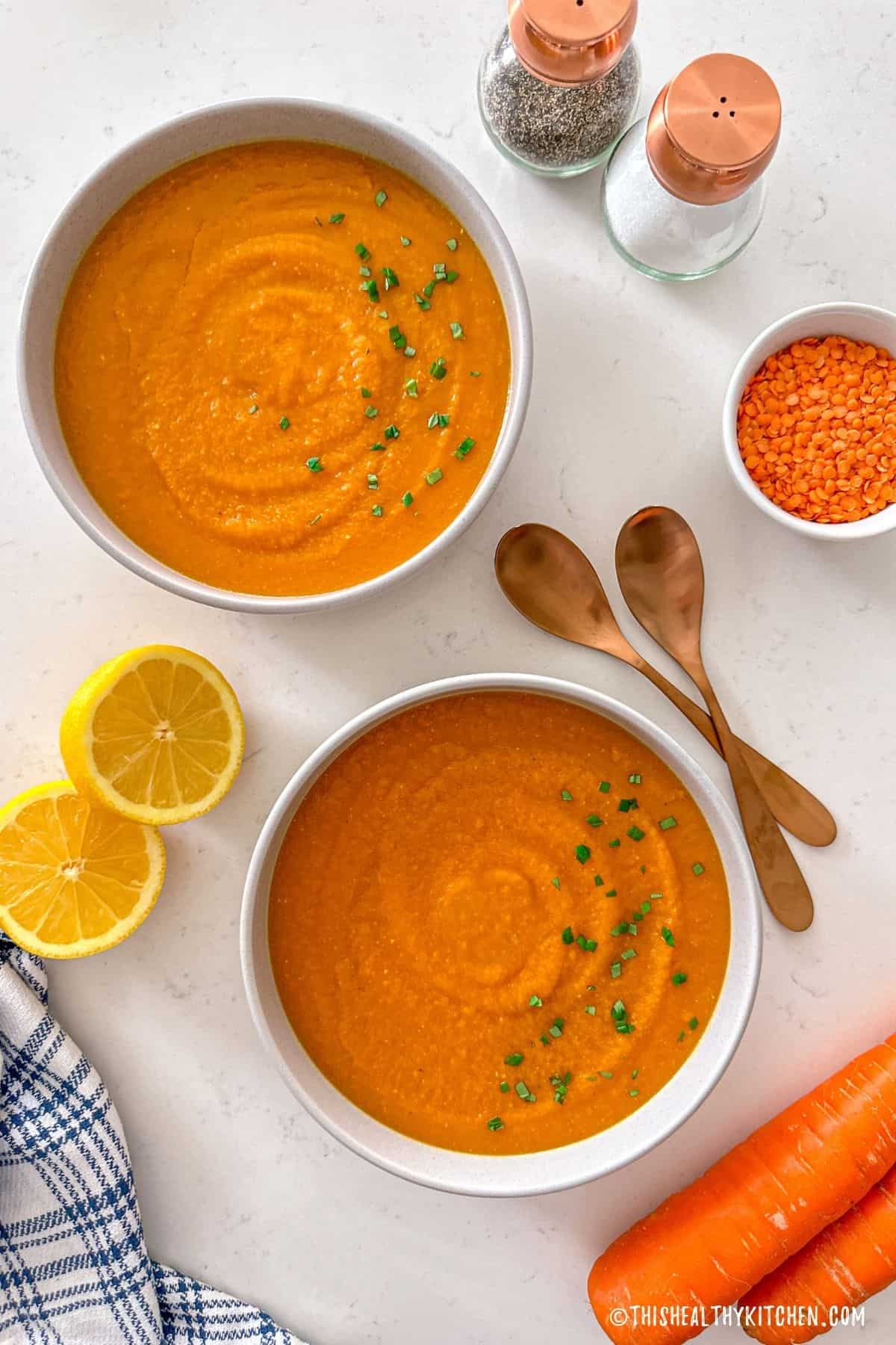 Two bowls of carrot lentil soup with lemons on the side.