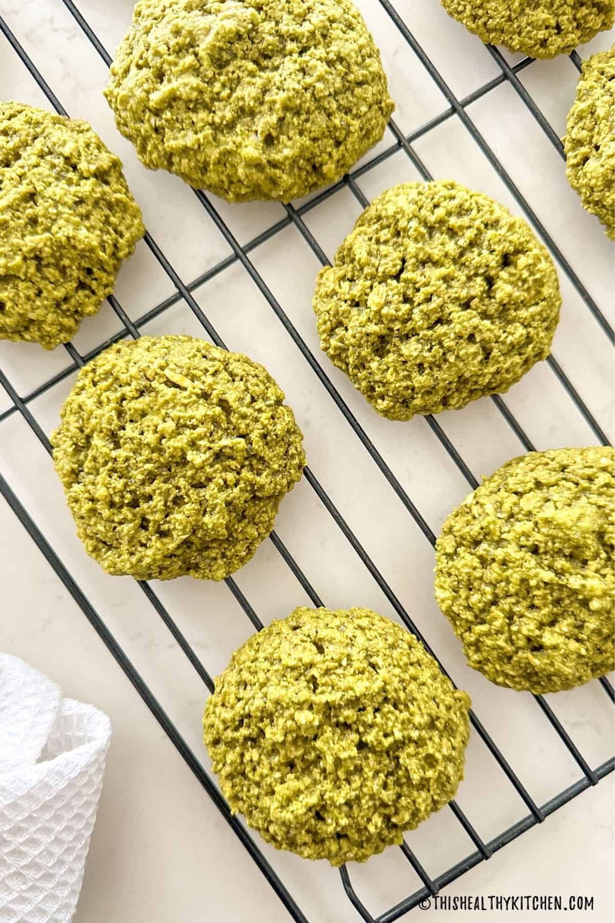 Vegan matcha cookies on wire rack with white towel beside it.