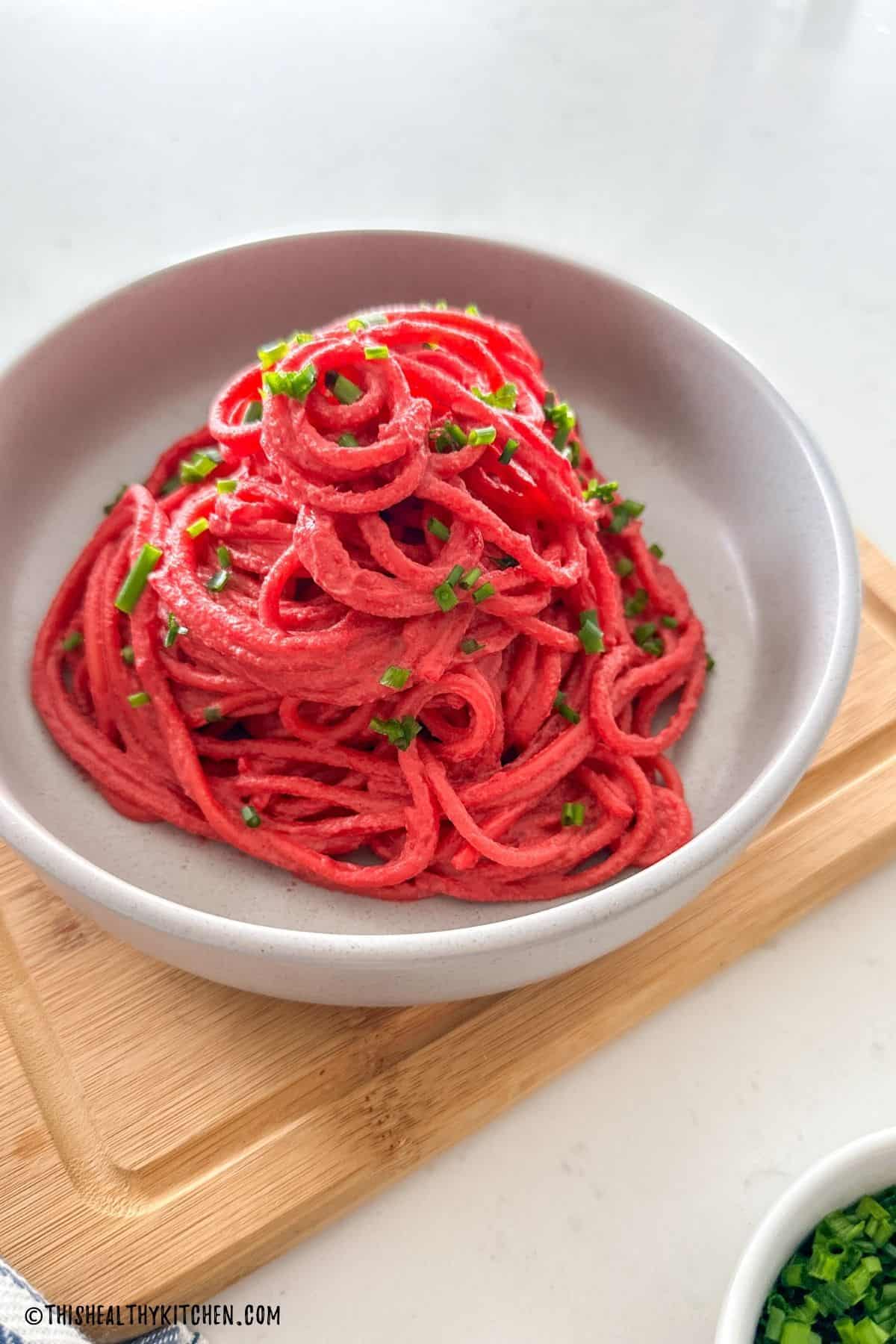 Grey bowl with spaghetti piled high with beet sauce and chives on top.